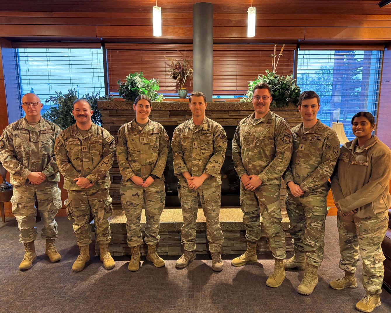 Indoor group photo of uniformed service members in front of a fireplace.